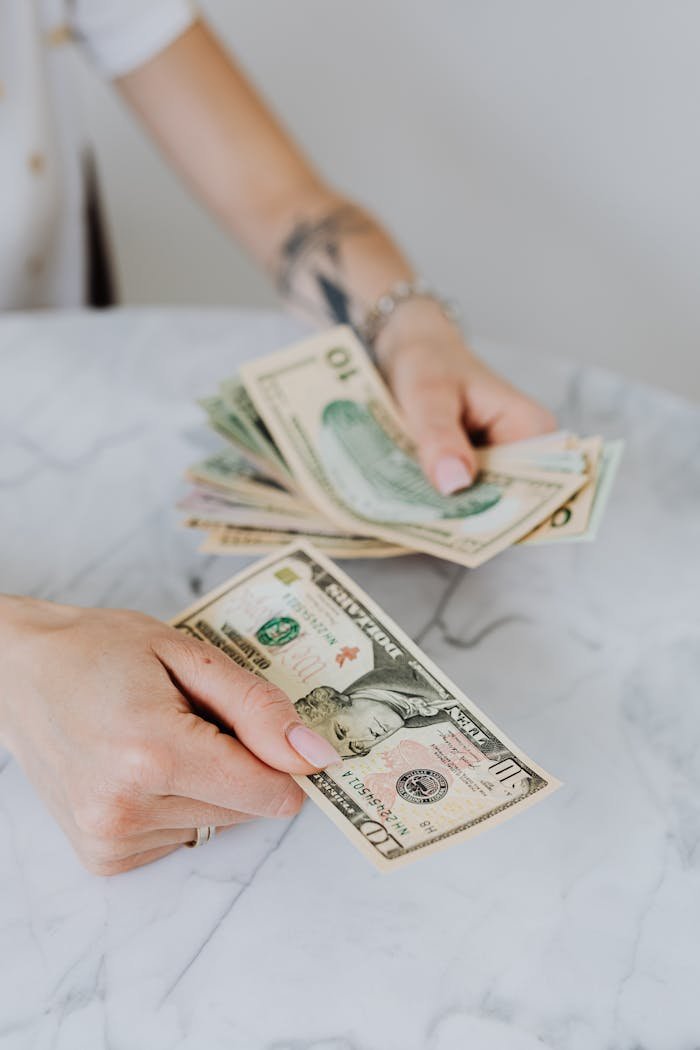 Close-up of hands counting US dollar bills on a marble table, symbolizing personal finance.